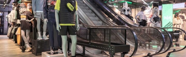 Display of athletic apparel on mannequins near an escalator in a retail store environment.