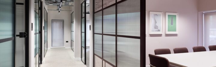 Interior view of a modern office corridor with glass partition walls and a conference table in a well-lit space.