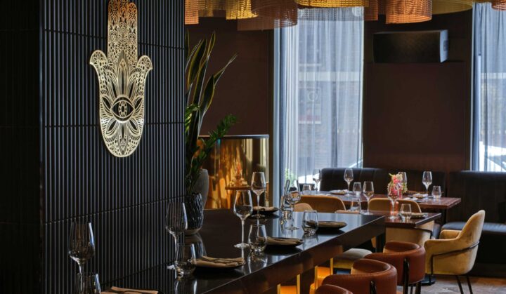 Interior view of a restaurant featuring a decorative wall with a hand symbol and elegant table settings with glassware.